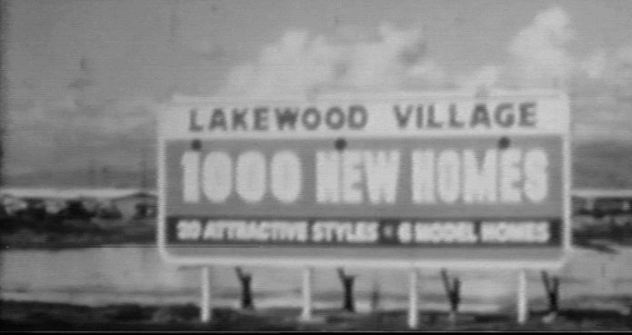A vintage photograph of a roadside billboard advertising Lakewood Village homes during construction in the mid-1950s.